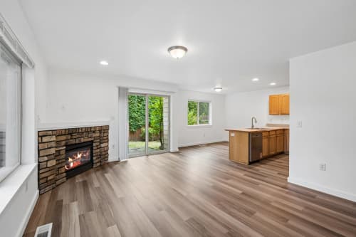 Open living room with stone fireplace, wood-look flooring, and patio door
